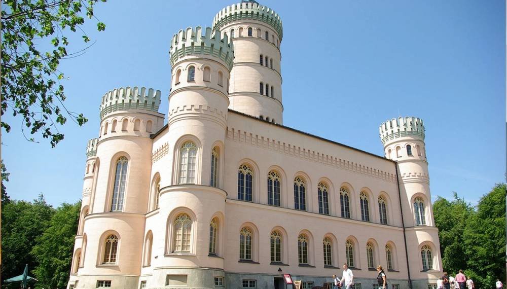 Helles Jagdschloss Granitz auf Rügen mit Rundtürmen und Besuchern bei Sonnenschein.
