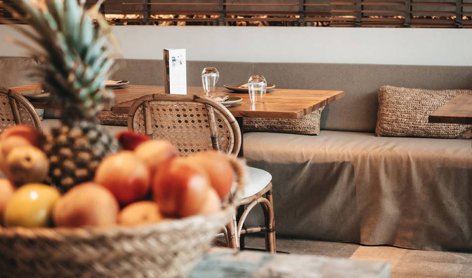 Ein Korb mit frischem Obst, darunter eine Ananas und Äpfel, steht auf einem Tisch im Restaurantbereich des Barefoot Hotels Mallorca.