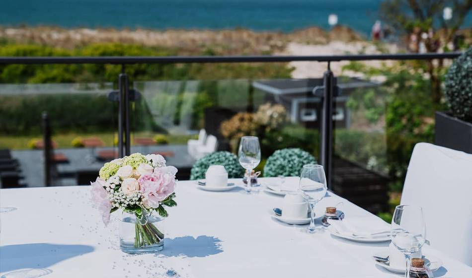 Festlich gedeckter Tisch mit Blumenarrangement und Weingläsern, im Hintergrund die Ostsee im Hotel Seezeichen.