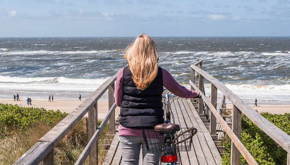 Frau mit Fahrrad an der Holztreppe am Westerländer Strand auf Sylt mit Blick auf die Nordsee