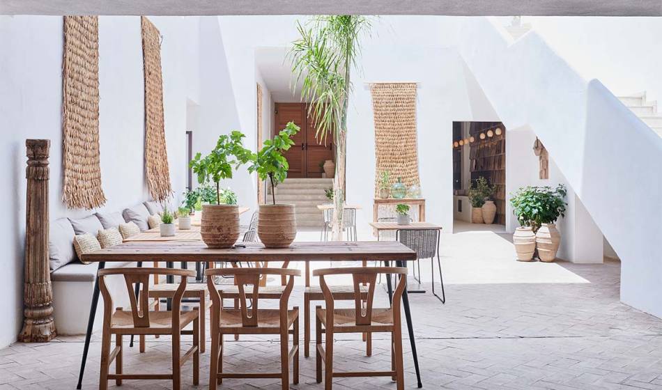 Großer Holztisch und Stühle, dekoriert mit Pflanzen, im stilvollen und sonnigen Innenhof des Barefoot Hotels Mallorca.