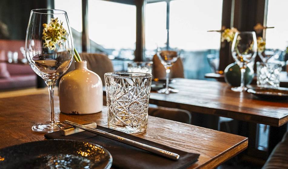Gedeckter Holztisch mit Weinglas, Wasserglas und Vase mit Blume im rustikalen Innenbereich des Restaurants #herrhoshi.