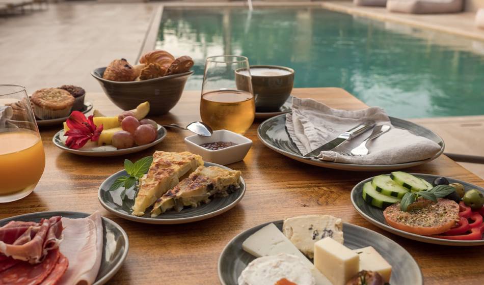 Auswahl an Käse, Schinken, frischem Obst und Getränken auf einem Frühstückstisch am Pool im Barefoot Hotel Mallorca.