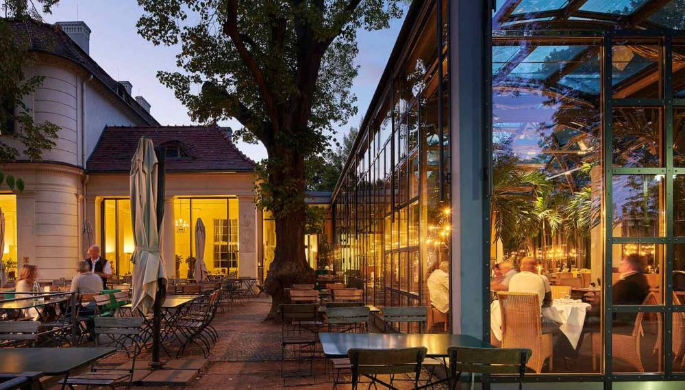 Abendliche Außenansicht des Restaurants Zur historischen Mühle mit Wintergarten, Gäste sitzen draußen und drinnen.