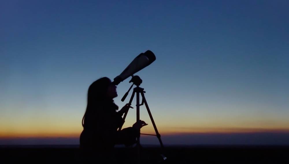 Frau bei Dämmerung beobachtet mit einem Fernrohr die Sonnenfinsternis auf Mallorca. © Adobe Stock, igorfp