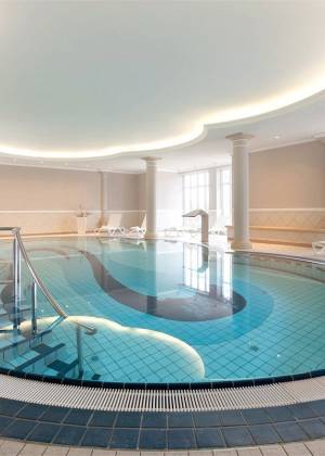 Heller Innenpool im Vju Hotel Rügen mit Säulen, Liegen und ruhiger Wellness Atmosphäre.