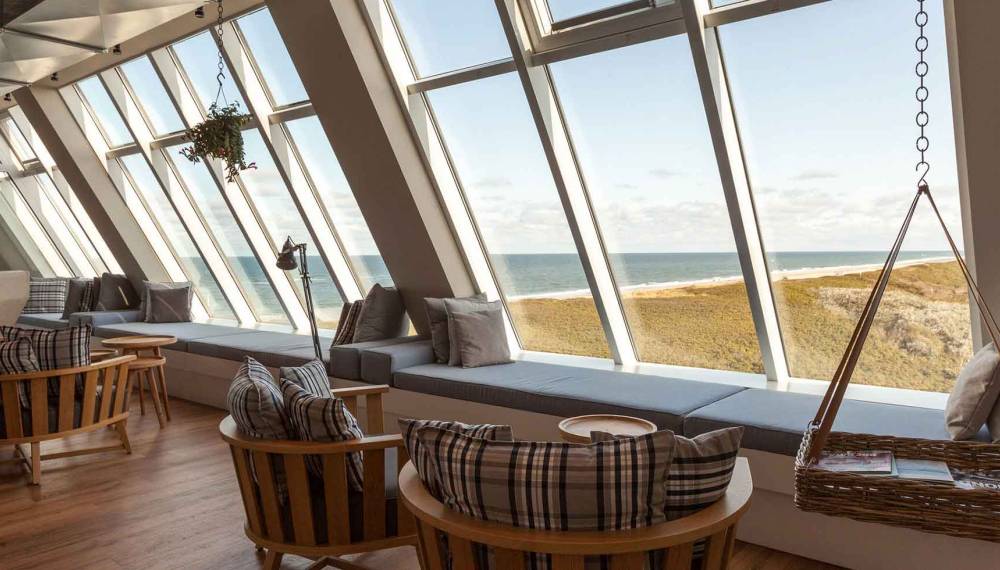 Gemütliche Lounge im Wellnessbereich mit Holzsesseln, Hängesessel und Panoramafenstern mit Blick aufs Meer.