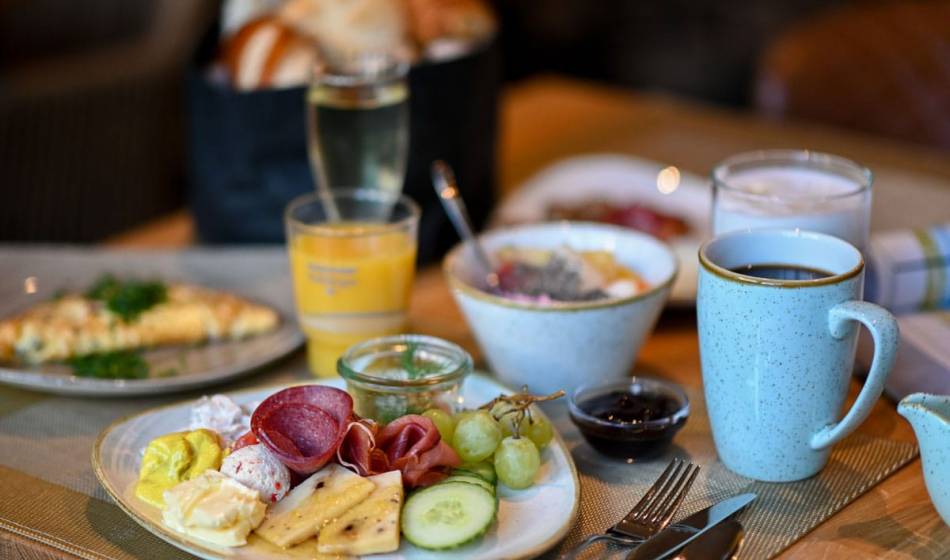 Reich gedeckter Frühstückstisch im Vju Hotel Rügen mit Käseplatte, Wurst, Obst, Joghurt und Kaffee.