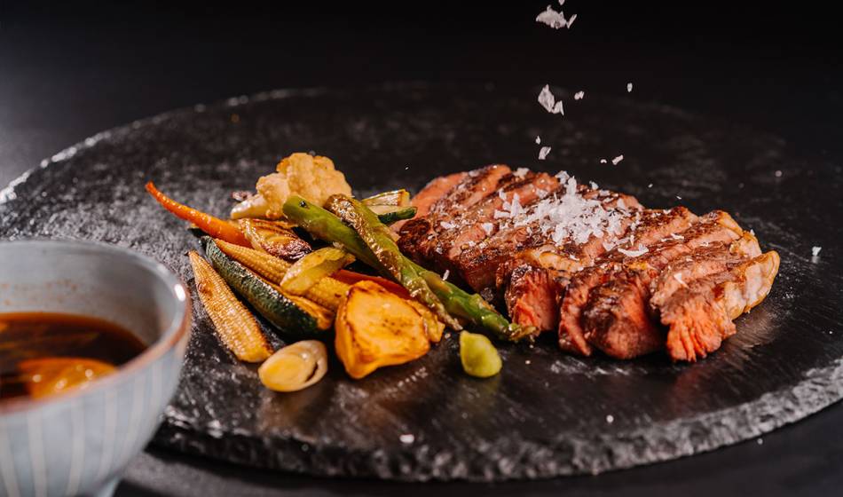 Zartes Entrecôte, serviert mit gegrilltem Gemüse wie Karotten und Bohnen, bestreut mit Meersalz, daneben Sauce im #herrhoshi.