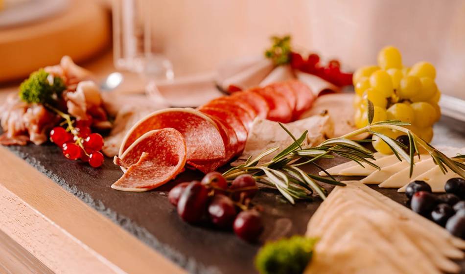 Schieferplatte mit einer Auswahl an Käse, Aufschnitt, Trauben und Rosmarin dekoriert, im #fraukorn im Hotel Seezeichen serviert.