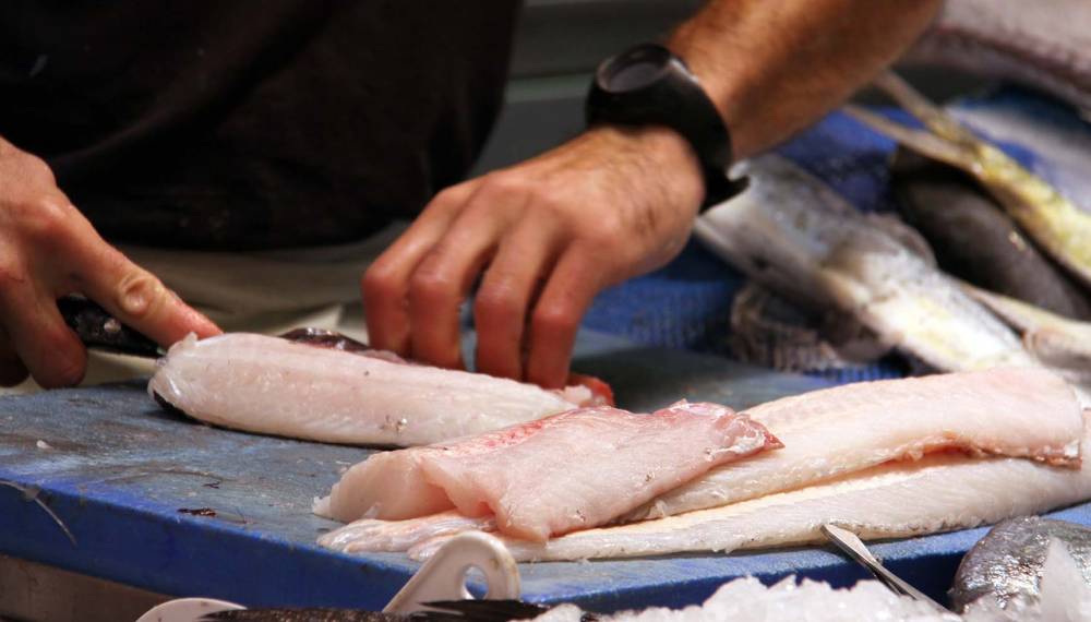 Ein Fischhändler filetiert frischen Fisch auf einem blauen Schneidebrett auf einem Fischmarkt.