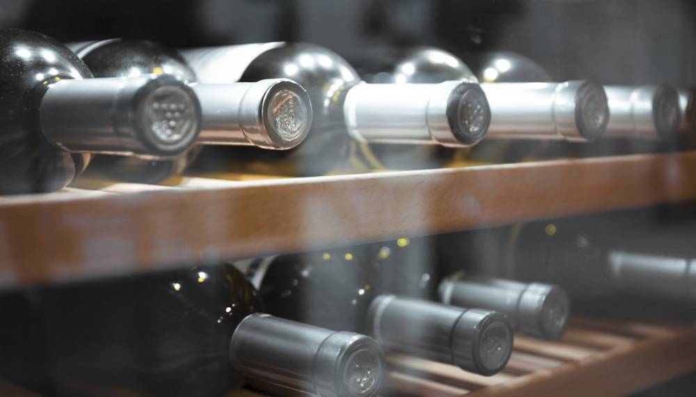 Mehrere Weinflaschen liegen horizontal in einem hölzernen Weinregal und werden kühl gelagert.
