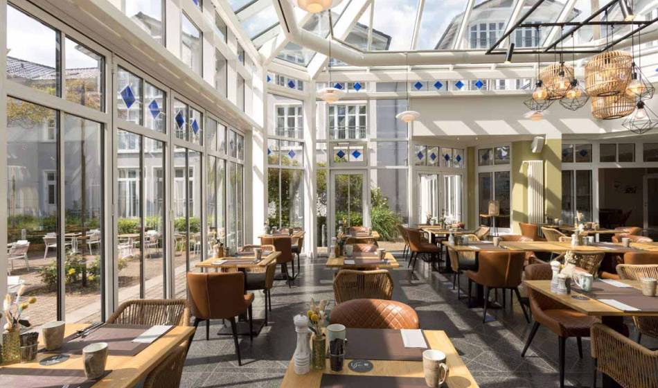 Einladender Wintergarten des Strandläufer Restaurants auf Rügen mit eleganter Einrichtung, Glasdach und hellem Ambiente.