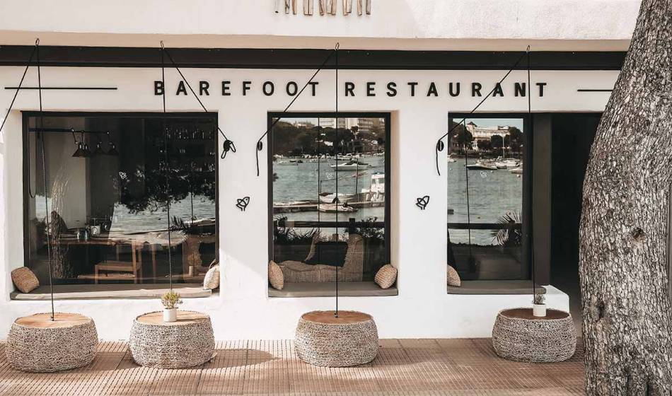 Außenansicht des Barefoot Restaurants Mallorca mit bequemen Sitzmöglichkeiten und Panoramablick durch die großen Fenster auf den Hafen.