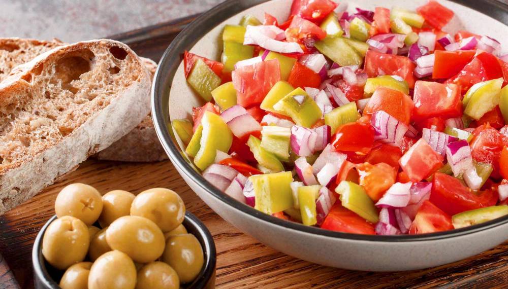 Typischer mallorquinischer Salat mit Brot und Oliven als Beilage, serviert auf einem rustikalen Holztisch