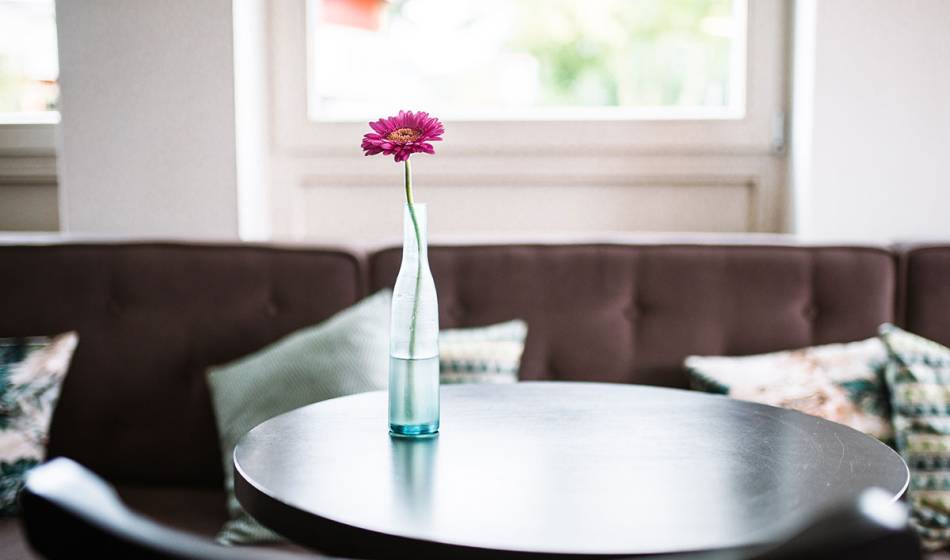 Nahaufnahme eines runden Tisches mit Vase und Einzelblume im Café #faukorn des Hotels Künstlerquartier Seezeichen.