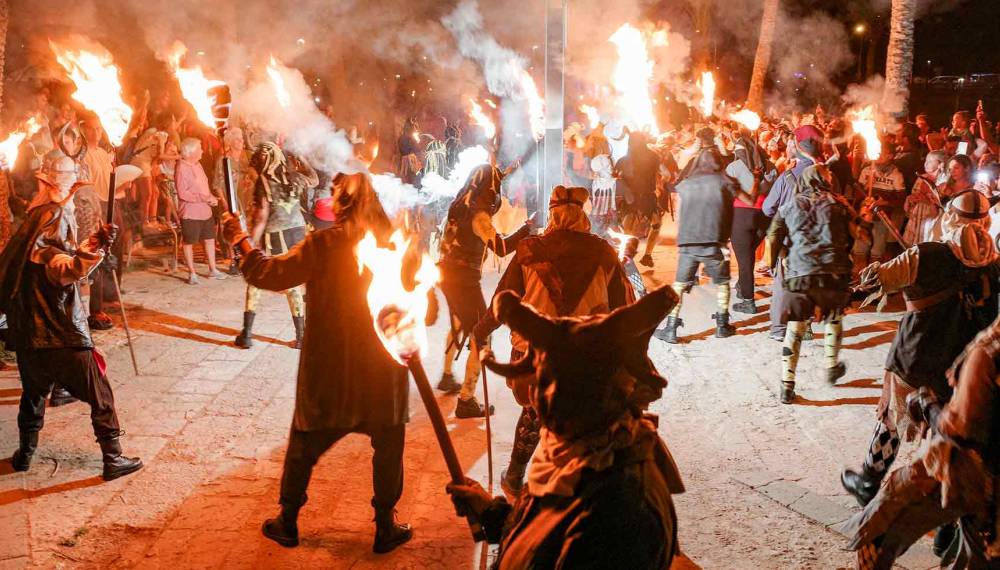 Kostümierte Teufelsfiguren mit brennenden Fackeln tanzen nachts inmitten von Rauch und Zuschauern bei einem traditionellen Feuerfest auf Mallorca