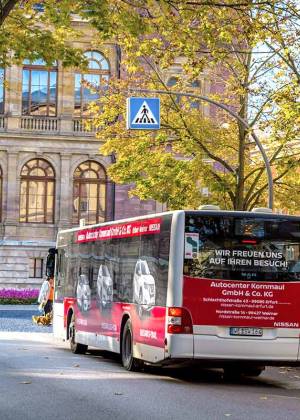 Kultur und Mobilität entspannt verbinden Stadtbus fährt auf einer von Bäumen gesäumten Straße vor einem historischen Gebäude in Weimar.
