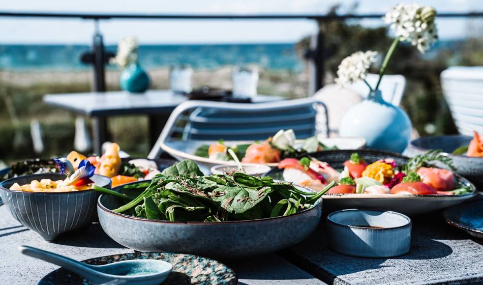 Verschiedene Teller mit frischen Speisen wie Salat, Sushi und Dips auf der Terrasse mit Meerblick im #herrhoshi.