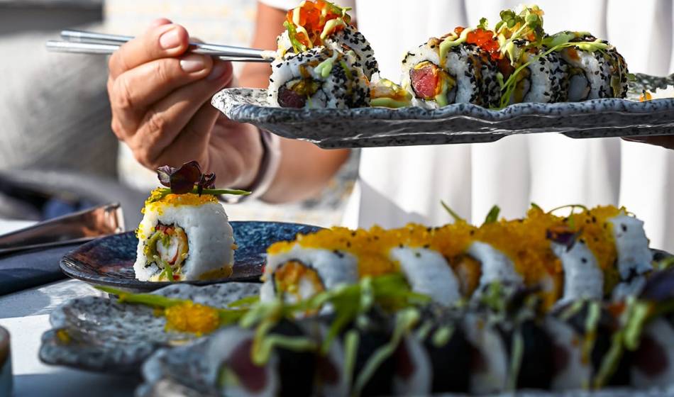 Hand mit Platte voll frischem Sushi vor weiteren sorgfältig arrangierten Sushi-Variationen im #herrhoshi Restaurant in Ahrenshoop.
