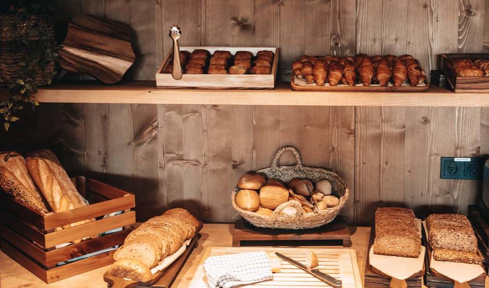 Verschiedene Brote, Brötchen und Croissants sind in einem rustikalen Holzregal zum Frühstück im Barefoot Hotel Mallorca ausgestellt.
