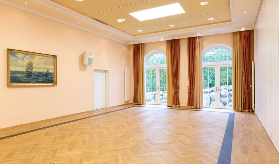 Großer, heller Veranstaltungsraum im Vju Hotel auf Rügen mit Holzboden, großen Fenstern und dezenter Wanddekoration, ideal für Events.