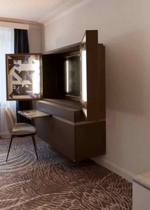 Zimmer im Hotel Elephant Weimar mit Sitzecke, Glastisch, Kunstwerken an der Wand, Schreibtisch mit TV-Schrank und Spiegel, in dem sich das Doppelbett zeigt