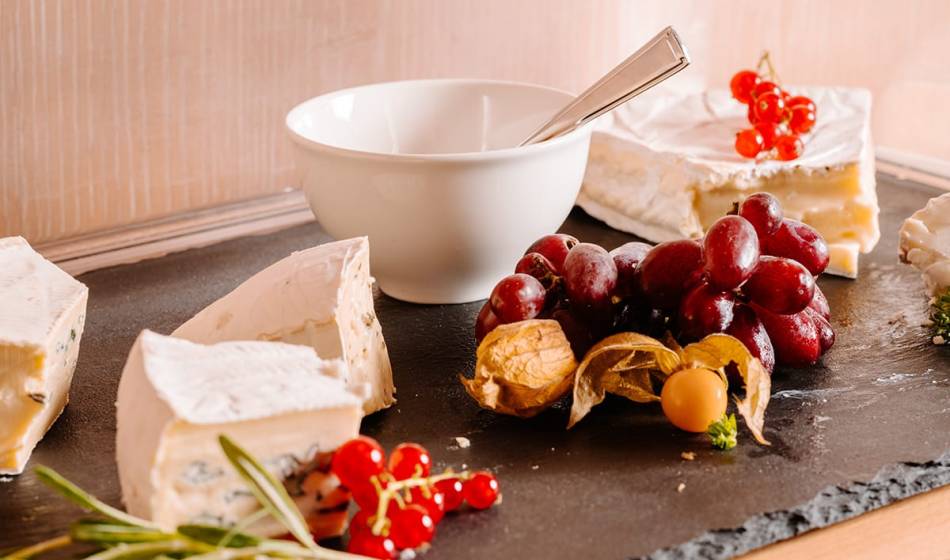 Eine Käseplatte mit Weichkäse, Trauben, Johannisbeeren und Physalis auf einer Schieferplatte im Künstlerquartier Seezeichen.