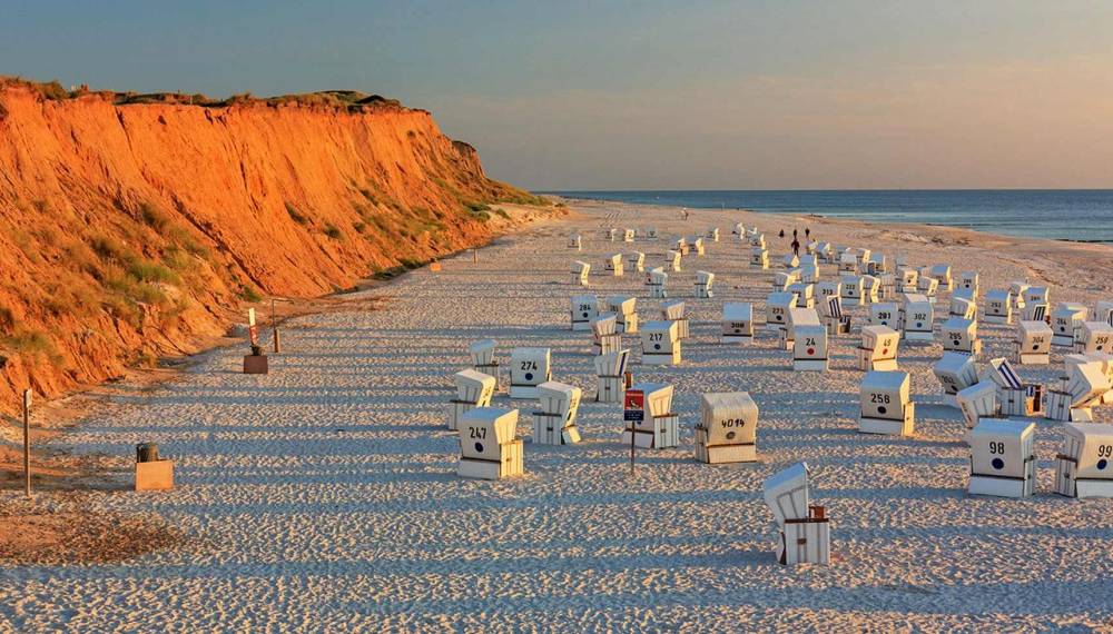 Strandkörbe am weißen Sandstrand vor dem leuchtend roten Kliff bei Abendlicht auf Sylt.