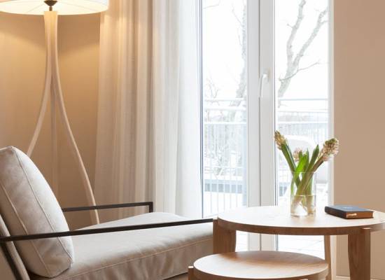 Moderne Sitzecke im Vju Hotel Rügen mit hellem Sessel, Holzbeistelltisch und großer Fensterfront.