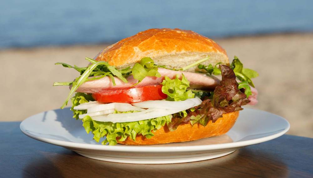 Usedomer Fischbrötchen mit knackigem Salat, serviert am Strand auf einem weißen Teller.