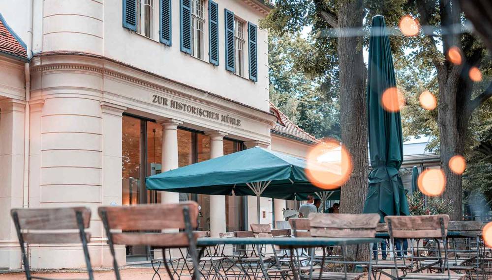 Tische und Stühle im Biergarten vor dem Gebäude der Gaststätte Zur historischen Mühle.