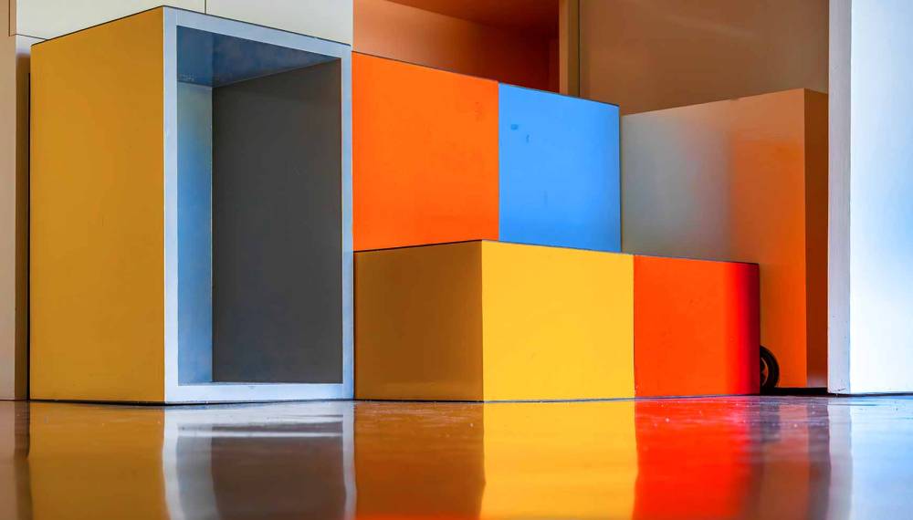 Farbige Kastenmöbel in Gelb, Orange, Blau und Weiß im Kinderzimmer des Bauhaus-Musterhauses Haus am Horn in Weimar, gespiegelt auf glänzendem Boden