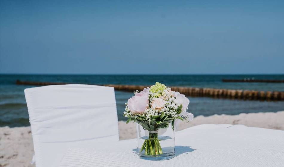 Eleganter Blumenstrauß auf weiß gedecktem Tisch vor dem Meer für eine Strandhochzeit an der Ostsee.