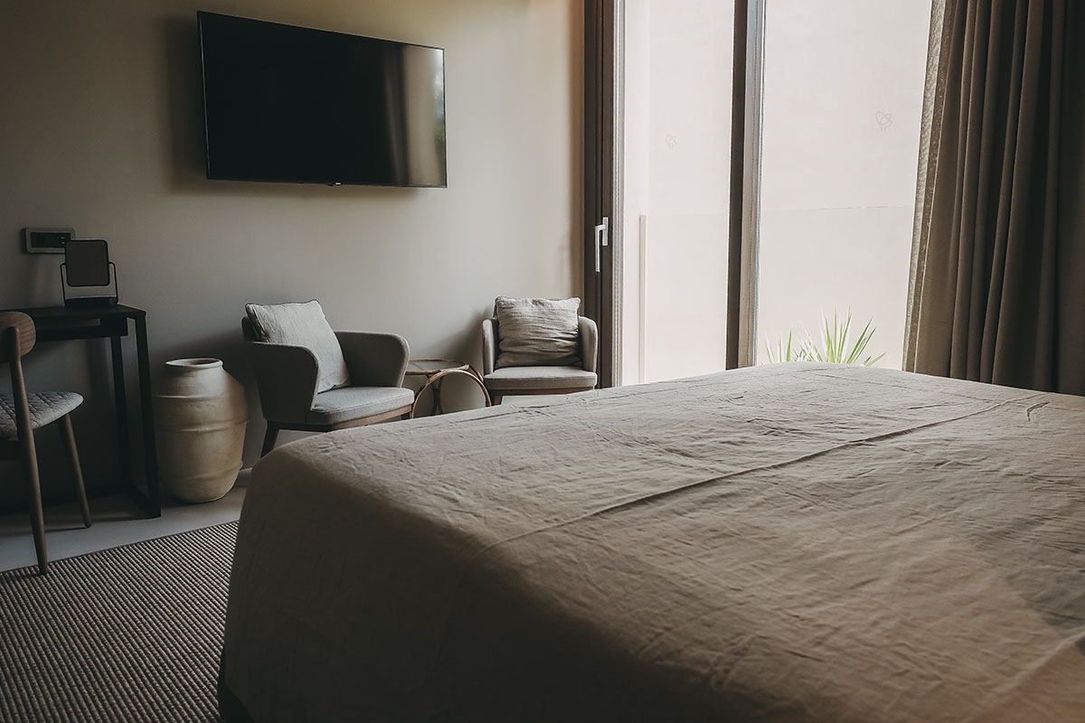 Blick in die Pequeña Suite des Barefoot Hotels Mallorca mit Bett, Sessel und Balkon, stilvolle Atmosphäre für deinen Aufenthalt.