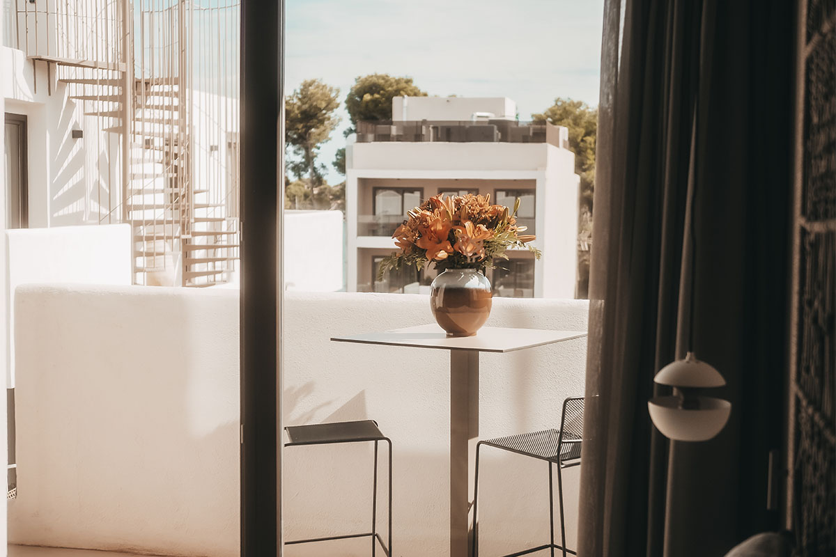 Eleganter Balkon der Pequeña Suite mit Tisch, Blumenvase und Ausblick auf das Barefoot Hotel auf Mallorca.