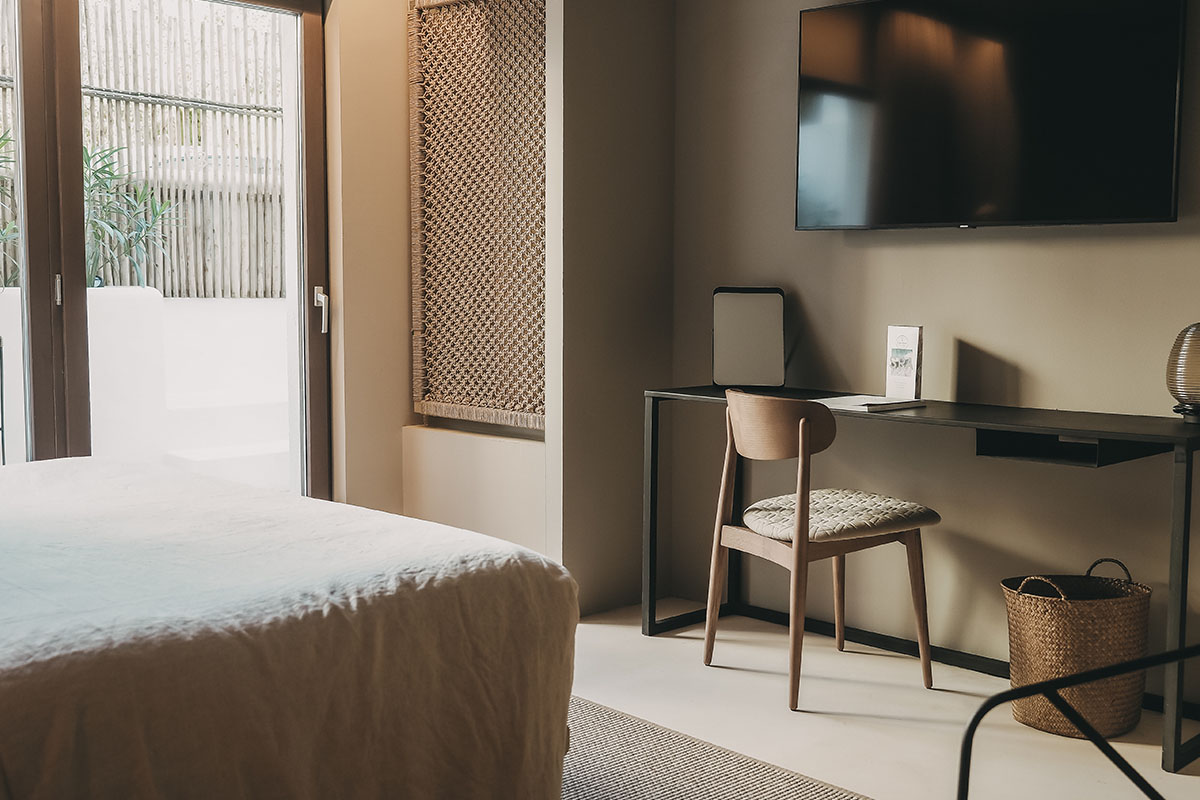 Moderner Arbeitsbereich im Zimmer Pueblo des Barefoot Hotel Mallorca mit Schreibtisch und Holzstuhl.