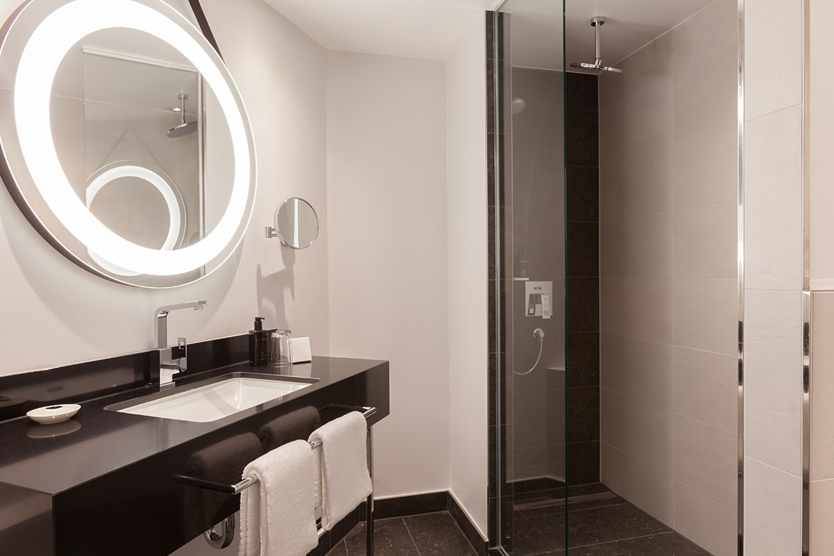 Modernes Badezimmer in der Junior-Suite des Hotel Elephant Weimar mit eleganter Dusche und beleuchtetem Spiegel.