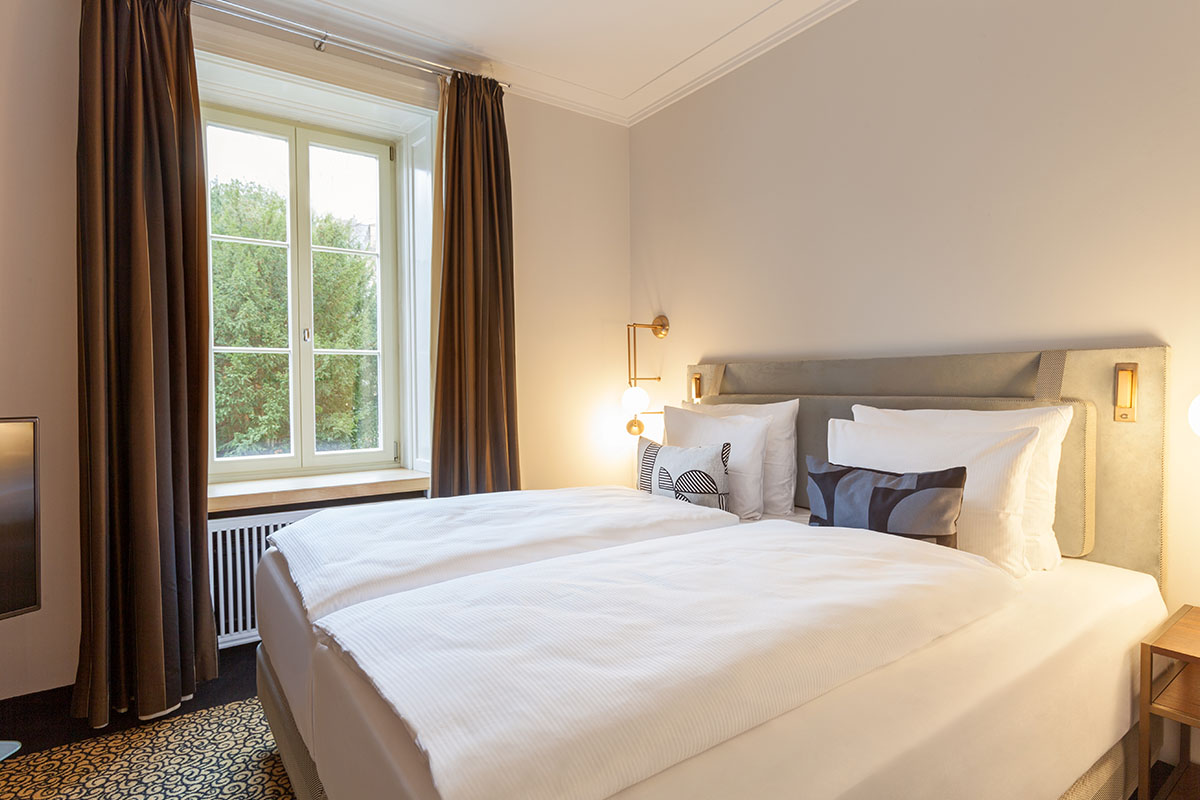 Komfortables Doppelbett mit luxuriöser Bettwäsche und dezenten Farbakzenten in der Thomas Mann Suite im Hotel Elephant.
