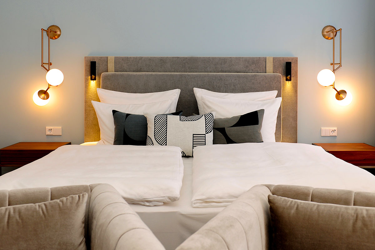 Modernes Doppelbett im Grand Deluxe Zimmer des Hotel Elephant Weimar mit eleganter Beleuchtung und weichen Kissen.