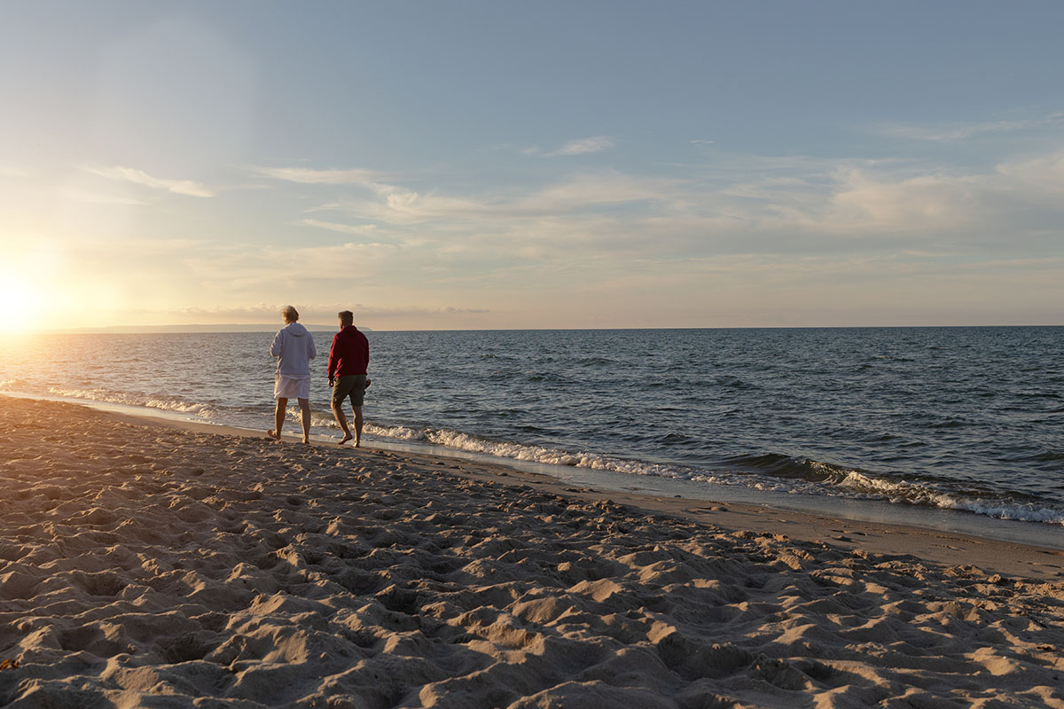 Zwei Personen spazieren barfuß am Strand dem Sonnenuntergang entgegen im Herbsturlaub im Koopmanns Hotel.