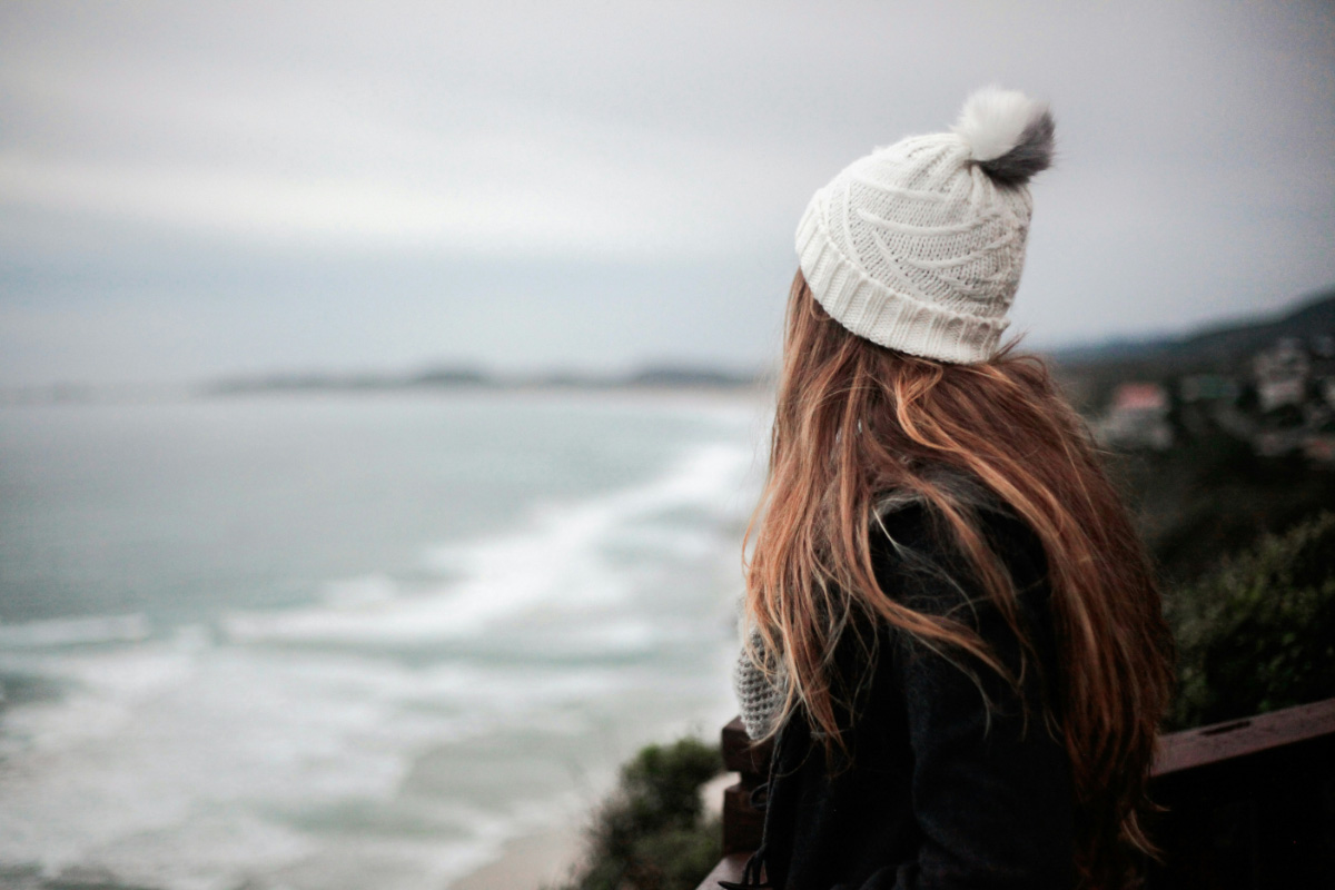 Frau mit Mütze blickt von einer Anhöhe auf die Ostsee und die Küstenlandschaft auf Rügen bei herbstlicher Stimmung