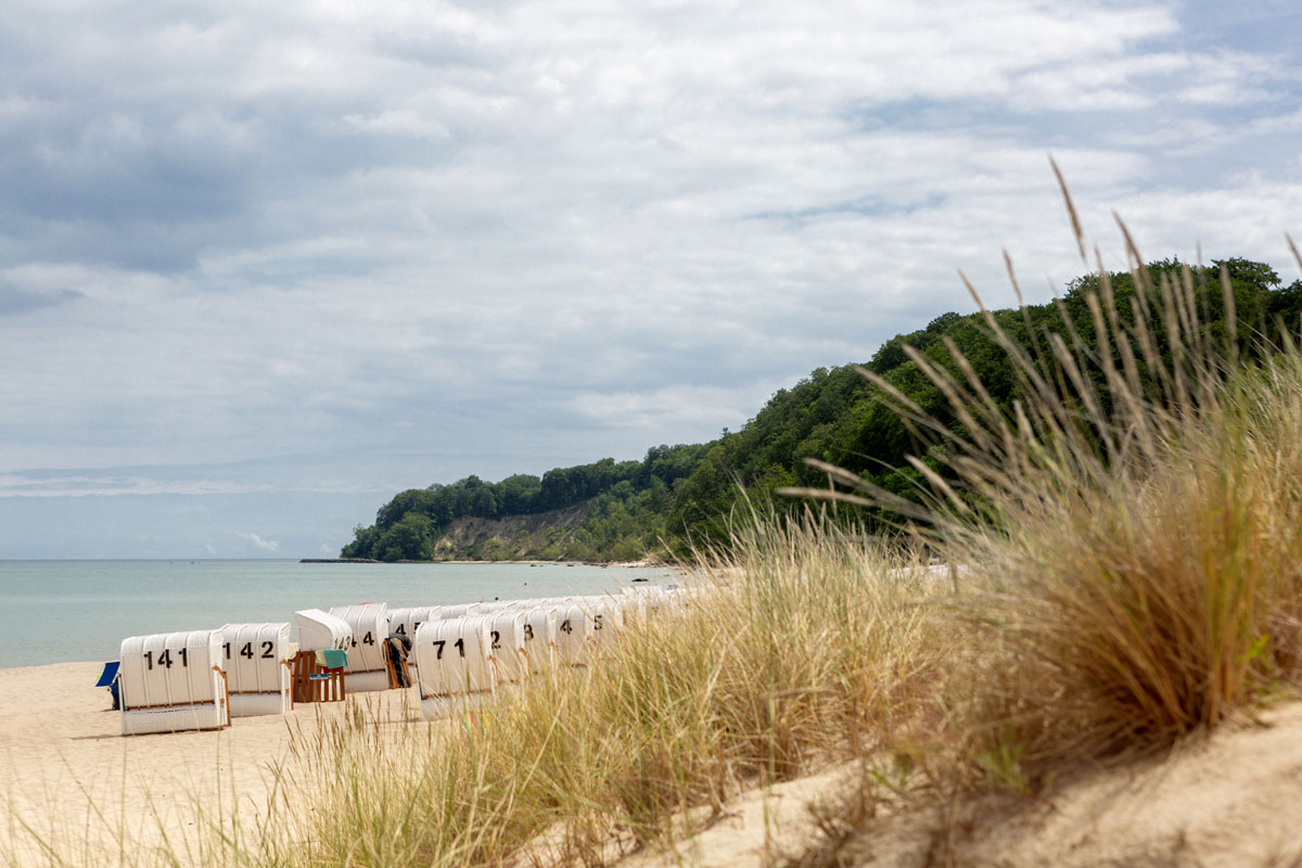 Sandstrand mit Strandkörben und Blick auf die grüne Steilküste von Rügen im Urlaub im Koopmanns Hotel.