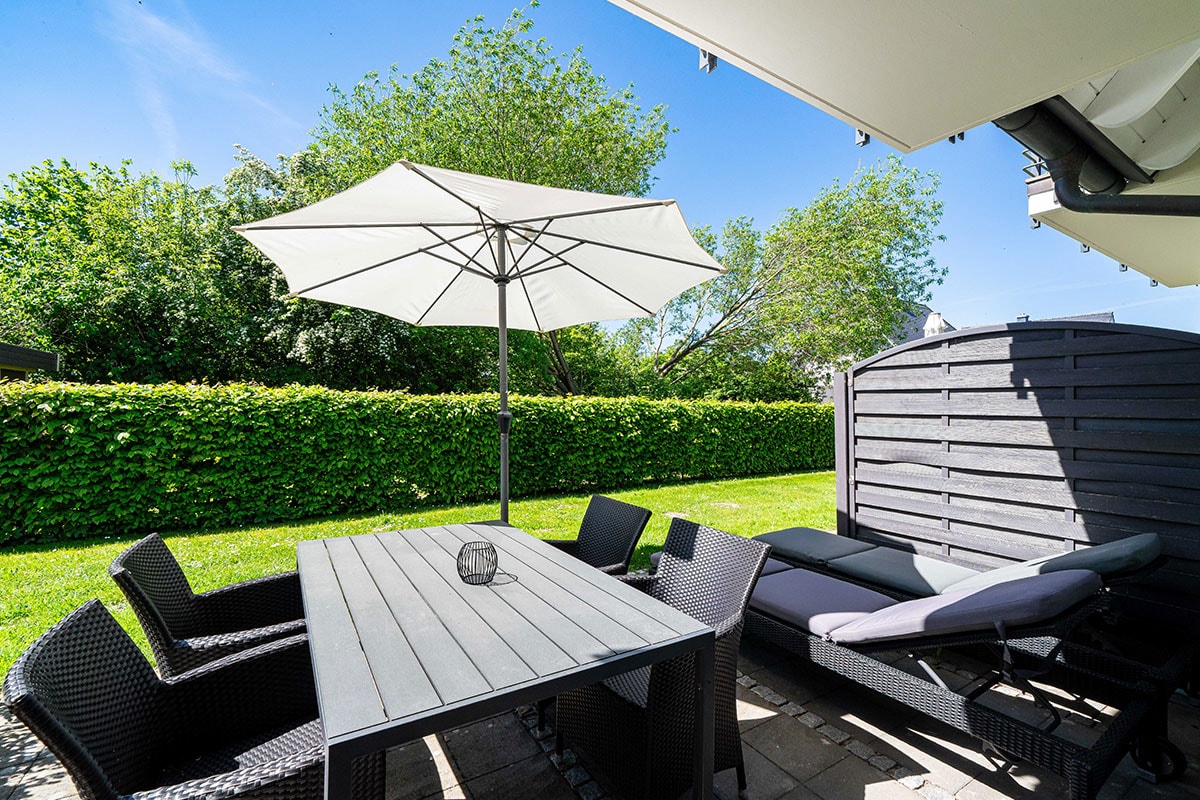 Private terrace of the Seeschwalbe vacation apartment in the Hotel Künstlerquartier Seezeichen with table, sun loungers and umbrella.