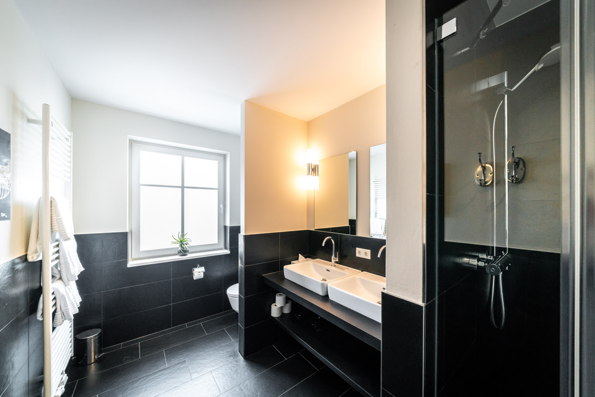 Badezimmer der Ferienwohnung Strandliebe im Hotel Künstlerquartier Seezeichen mit Doppelwaschbecken und Regendusche.