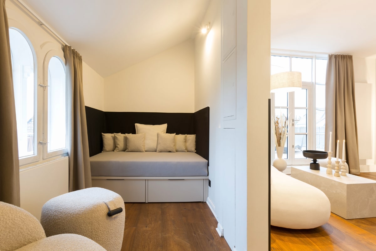 Bright day bed with cushions, flanked by large windows and curtains in the Elisabeth Suite in the Hotel Künstlerquartier Seezeichen.