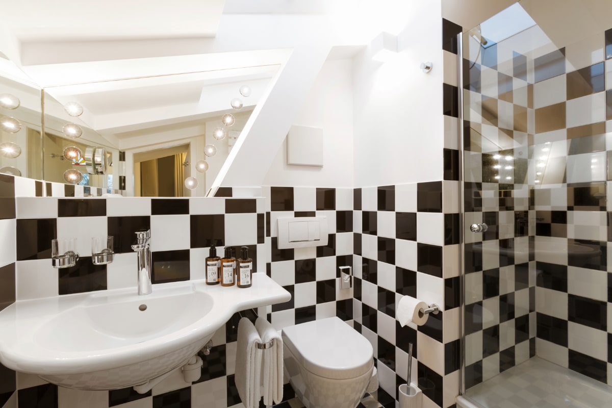 Modern bathroom with checkerboard tiles, shower, washbasin and stylish lighting in the Elisabeth von Eicken Hotel.