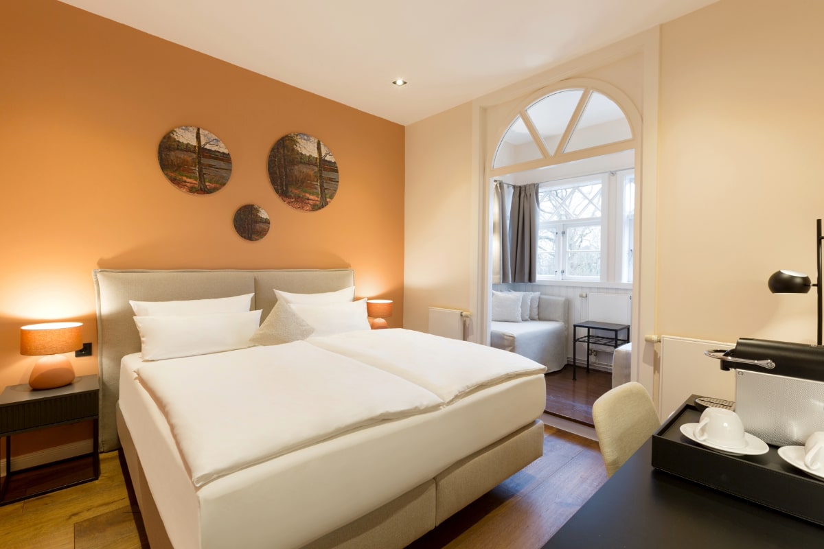 Double bed with elegant bedside tables and warm color accents in the double room with sea view at the Elisabeth von Eicken Hotel.