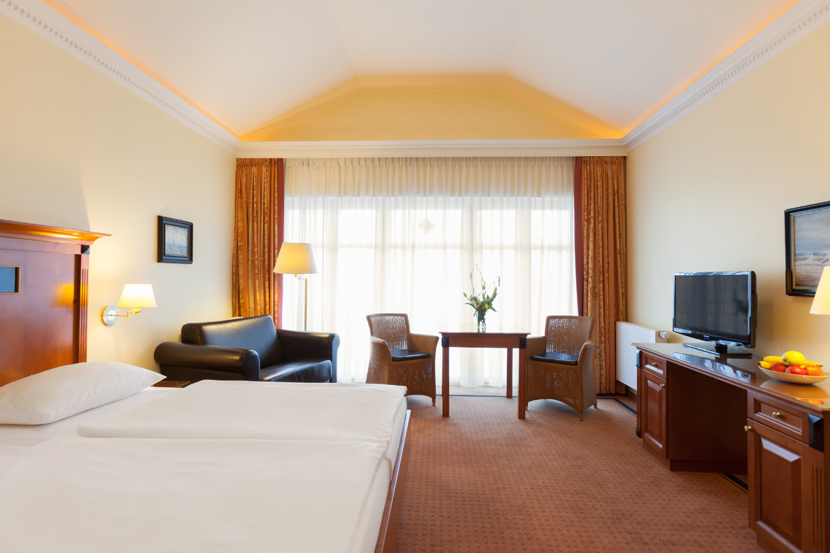 Lichtdurchflutetes Doppelzimmer im Vju Hotel mit eleganter Ausstattung, gemütlichem Bett, Sofa und Balkon.