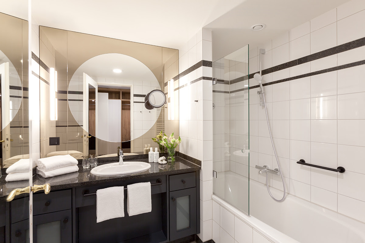 Helles Bad mit Glasdusche, großer Spiegelwand und schwarzen Akzenten im Doppelzimmer des Vju Hotels.